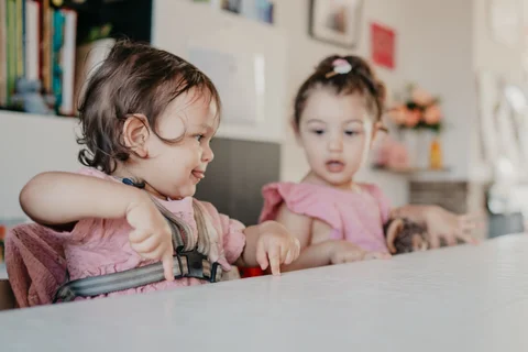 Een peuter in de kinderstoel speelt samen met een ouder kind aan tafel