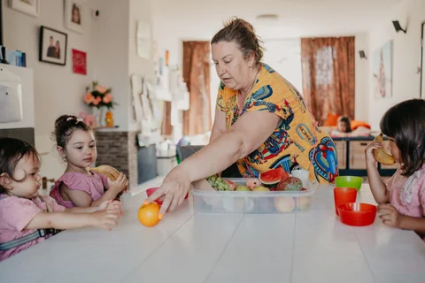 De gastouder maakt fruit klaar terwijl de kinderen aan tafel zitten