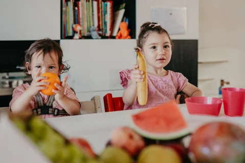 Een peuter in de kinderstoel houdt een banaan vast tijdens het fruitmoment