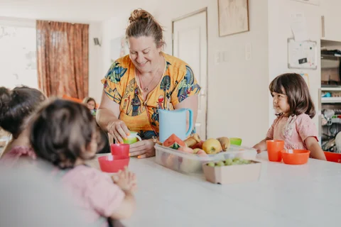 De gastouder helpt een kind met het fruitbakje aan tafel