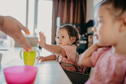 Een kind reikt naar iets op tafel vanuit de kinderstoel