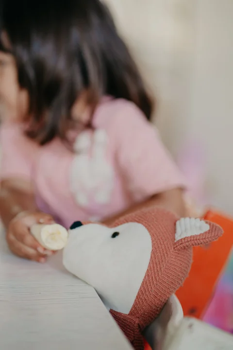 Een kind geeft de knuffelvos een stukje banaan aan tafel