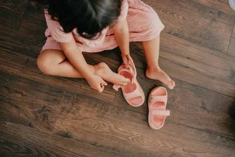 Een kind trekt de schoenen aan, zittend op de houten vloer