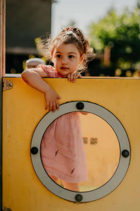 Een kind kijkt door een rond kijkgat van het speeltoestel