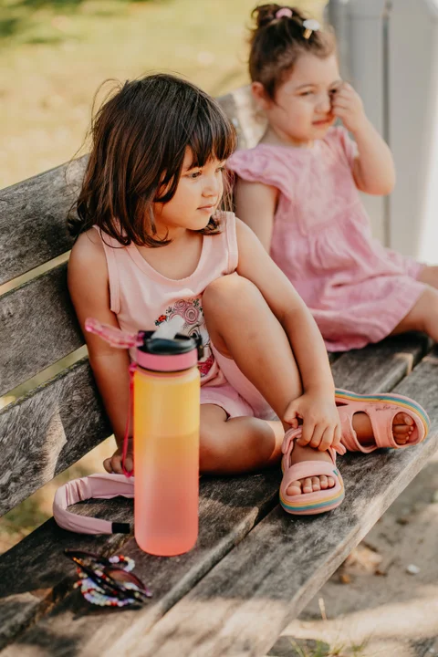 Twee kinderen rusten samen op een bankje met een drinkfles